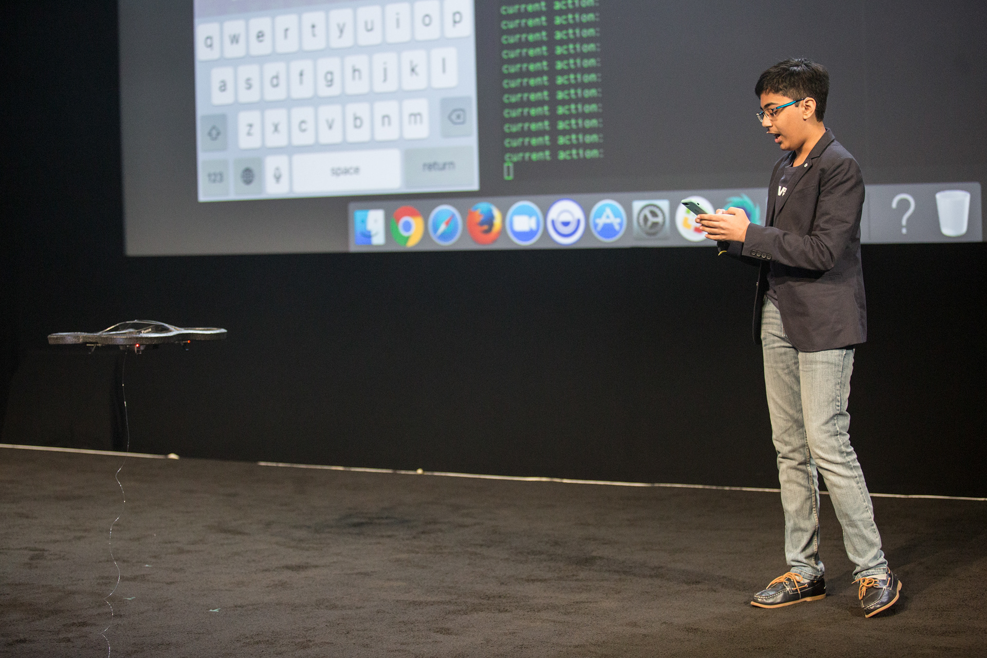 Young presenter controlling a drone on stage with code scrolling on backdrop